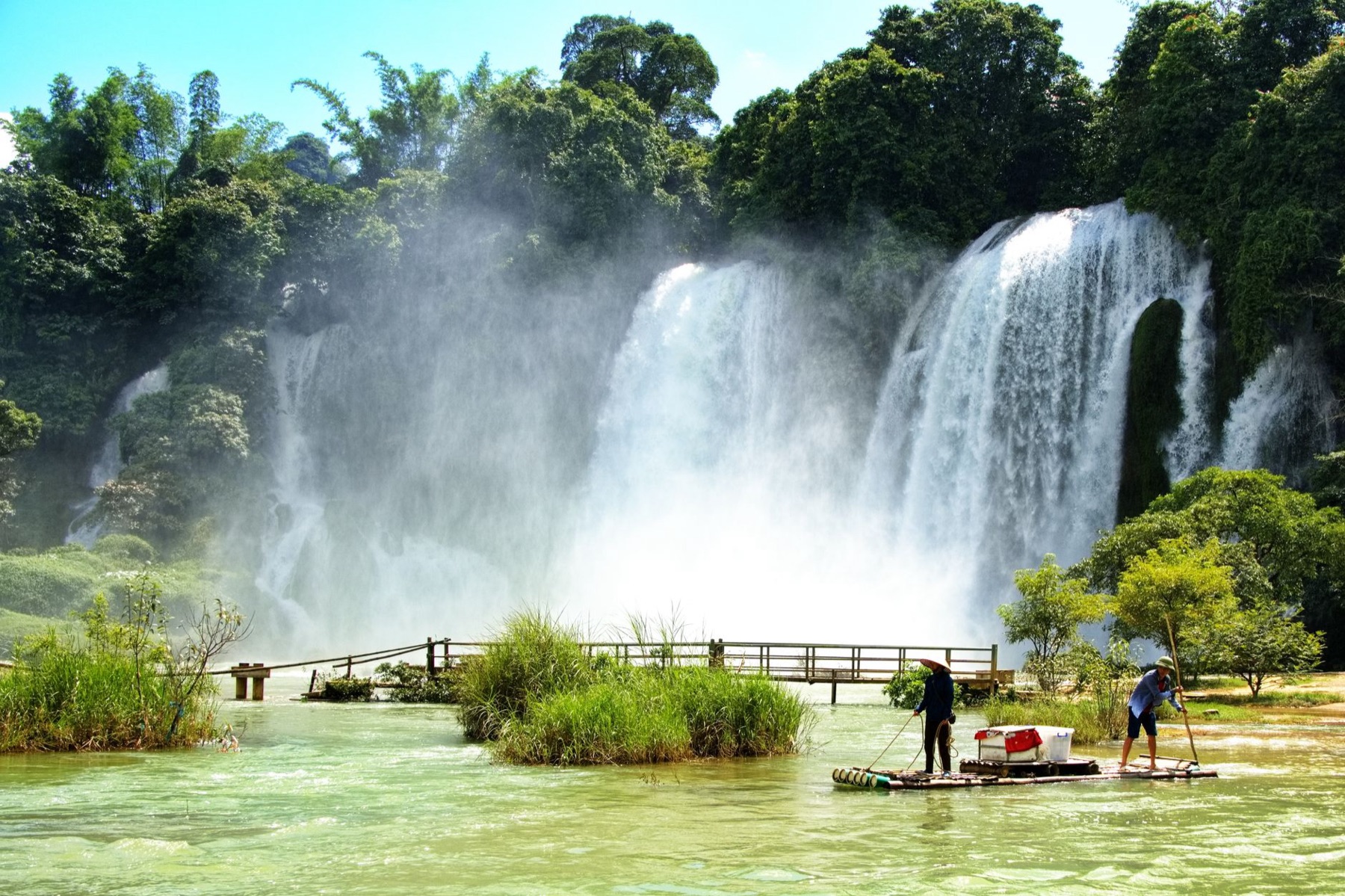Cao Bang — Beautiful waterfall with people rafting on a bamboo raft in a lush green setting
