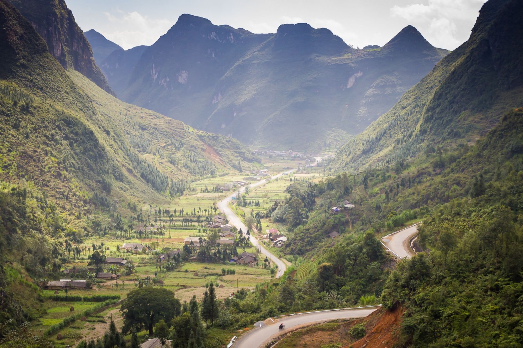 Ha Giang — Scenic mountain valley with winding roads and lush greenery during daylight.