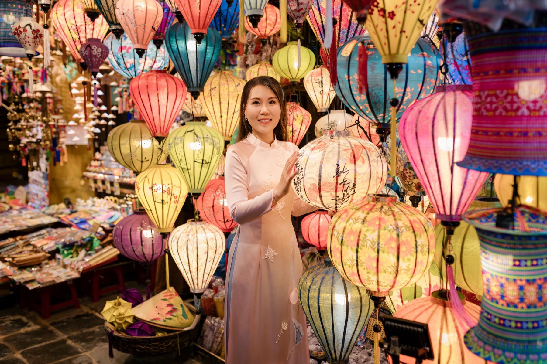 Hoi An — A woman in traditional Ao Dai surrounded by vibrant lanterns at a market in Hội