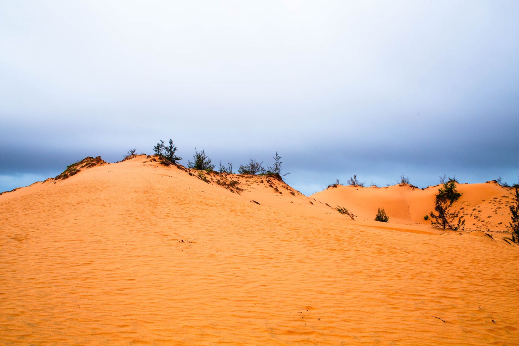 Mui Ne — Captivating scene of orange sand dunes against a dramatic cloudy backdrop, perfe