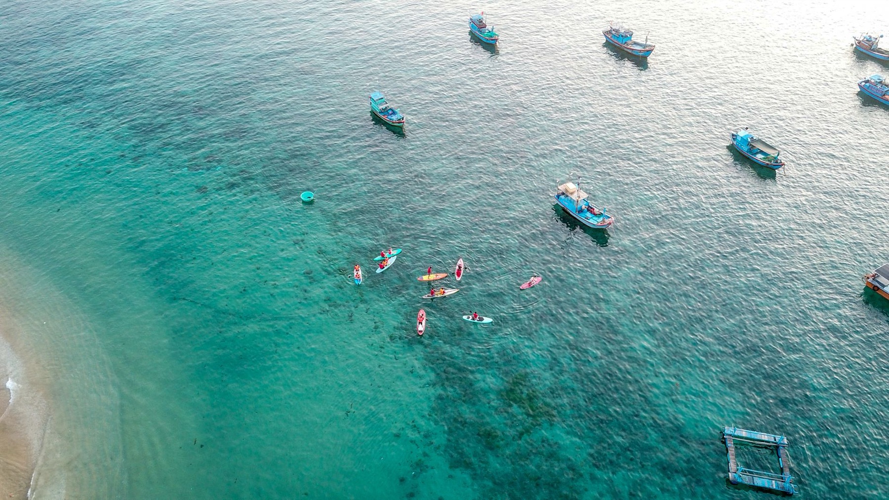 Quy Nhon — Aerial shot capturing vibrant boats and kayakers in clear turquoise waters of Qu